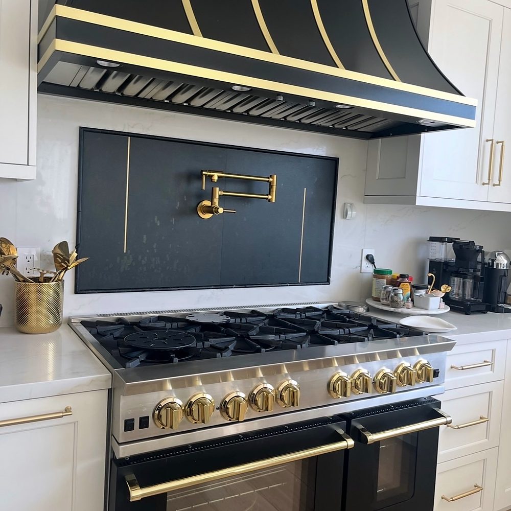 Brass wall-mounted pot filler installed above a six-burner range